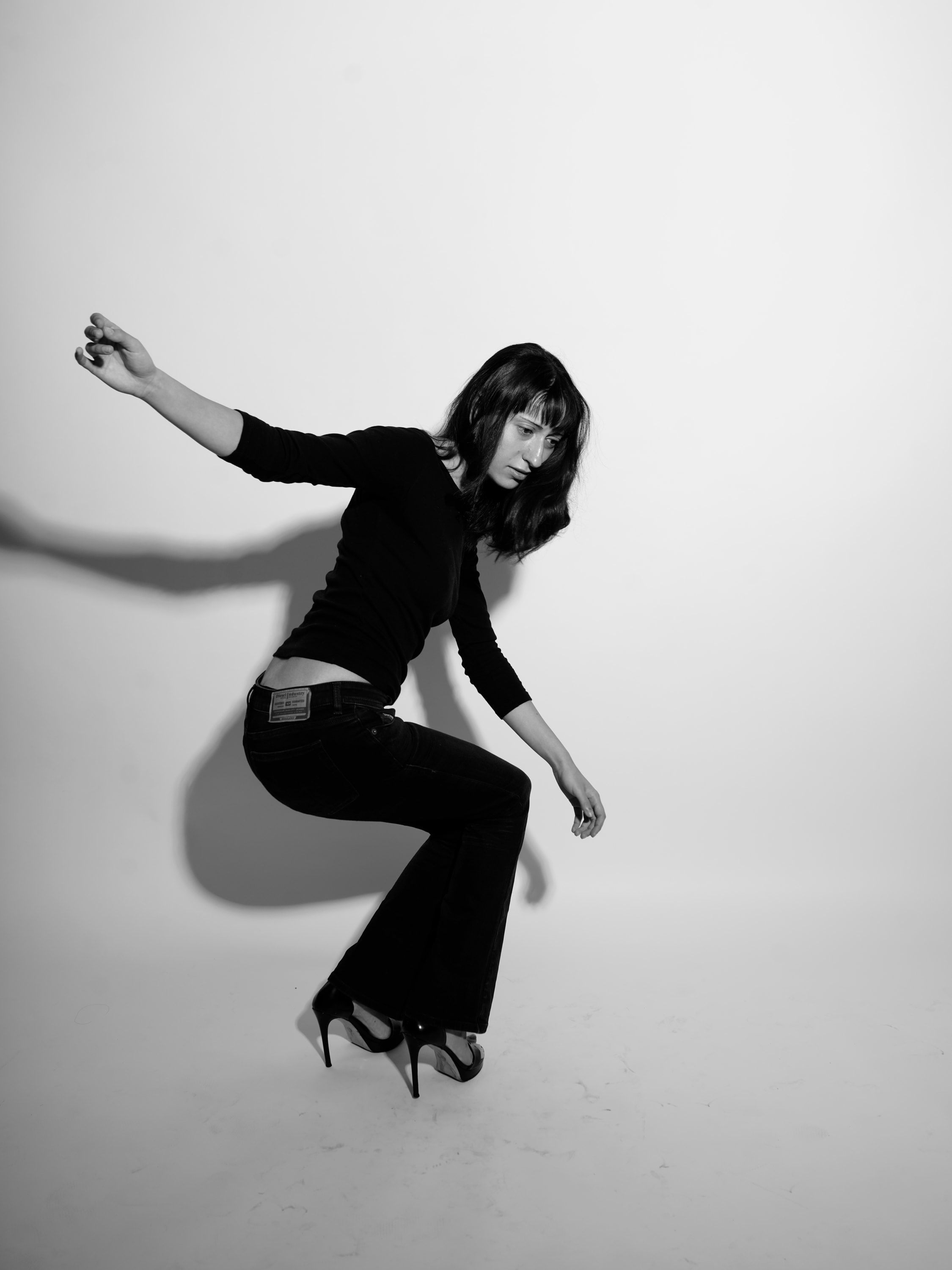Chrissa mid-movement on a white sweep, knees bent and one arm thrown out, in a black top and jeans.
